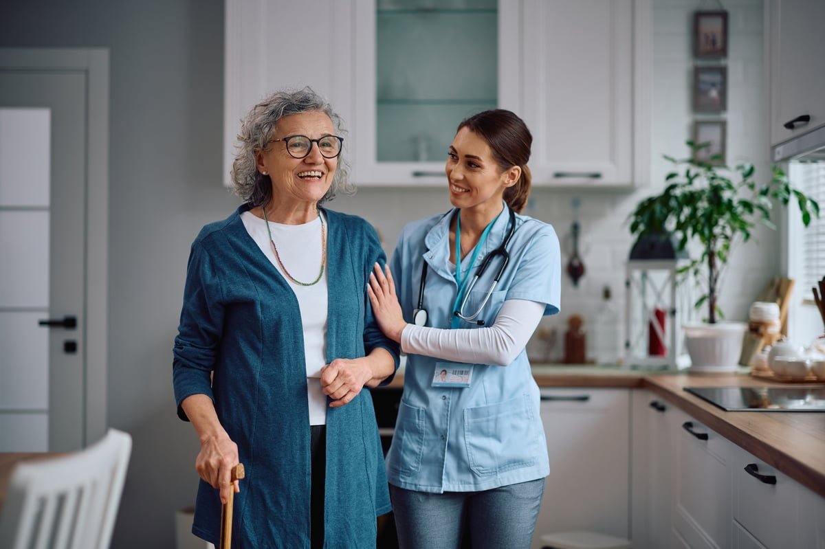 Happy home caregiver assisting her senior patient with walking