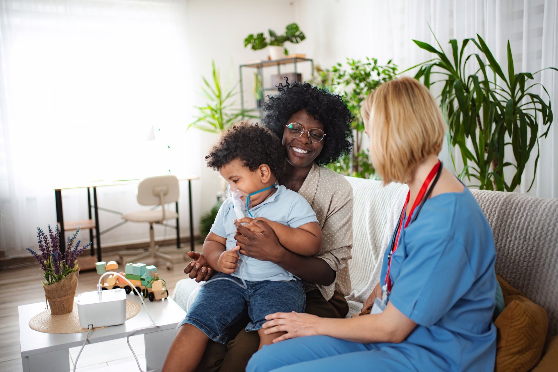 Nurse providing medical care to a child with a nebulizer while mother offers comfort at home