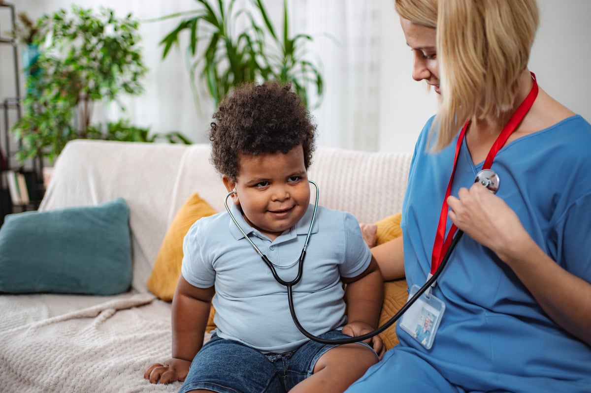 Pediatric nurse listening to child's heartbeat with stethoscope during a medical home visit